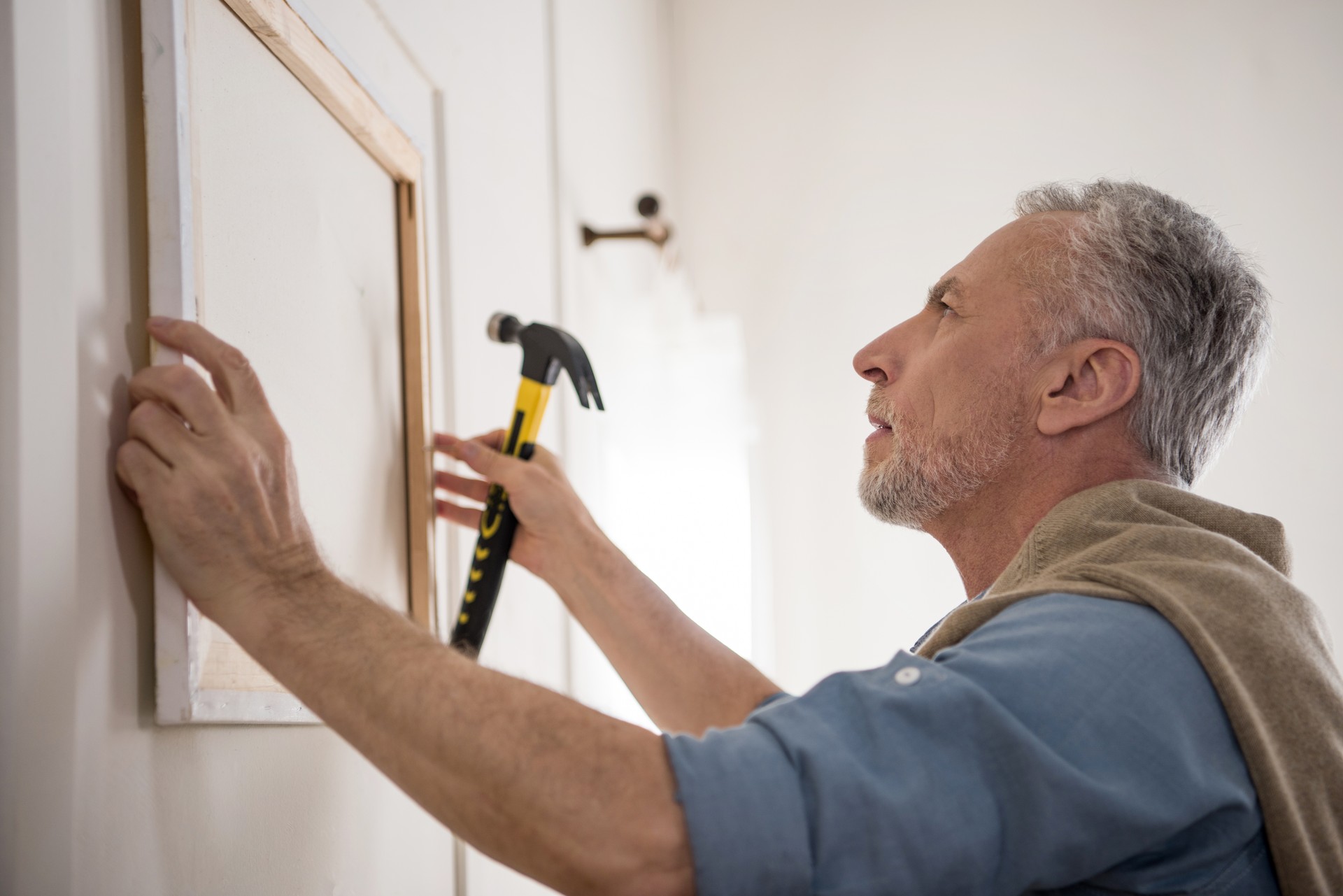 side view of focused senior man hanging picture on wall at new home